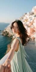 Naklejka premium Woman in flowing green dress leading partner along a coastal cliffside with white houses and sea view for travel wallpaper and vacation poster design