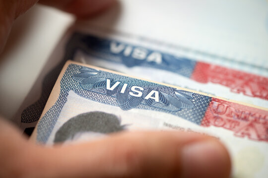 United States visa stamp inside an open passport document, held by a hand, for immigration, international travel, border security, visa application, and citizenship topics.