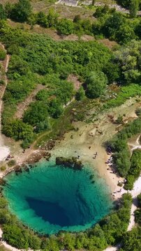 Aerial view of the Cetina River spring, a deep karst water source in Croatia, with tourists exploring the turquoise pool and surrounding nature