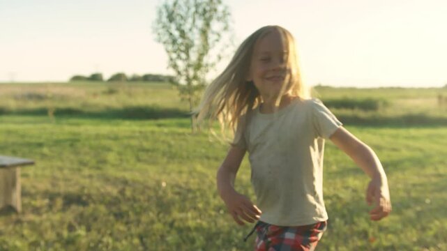 Boy running into sunset across green field with arms outstretched at golden hour