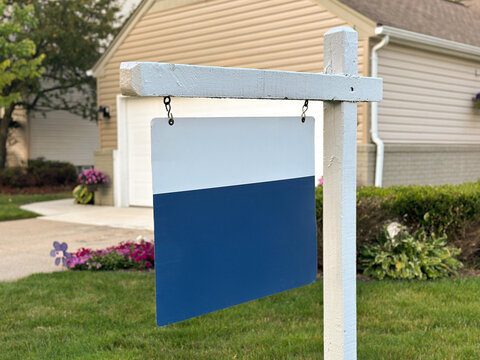 A blank real estate sign hangs in front of a suburban home, surrounded by a landscaped lawn, driveway, and garage. Ideal for property, housing, real estate, and neighborhood concepts.