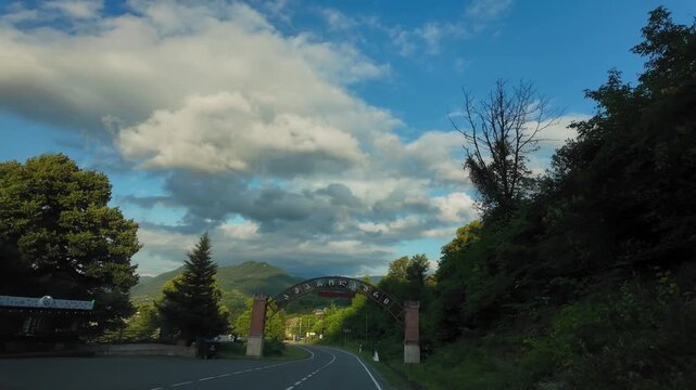 Scenic car ride on a winding asphalt road through the mountainous landscape, passing under the welcome arch of ambrolauri city in the racha region of georgia on a partly cloudy day