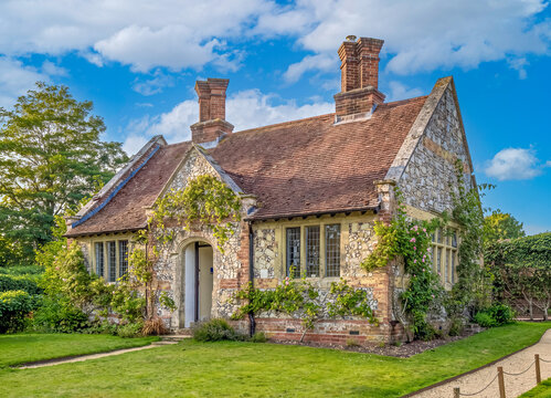 Ein charmantes, altes Landhaus aus Naturstein und Backstein mit Kletterpflanzen, umgeben von einem gr&uuml;nen Garten an einem sonnigen Sommertag in Hampshire.