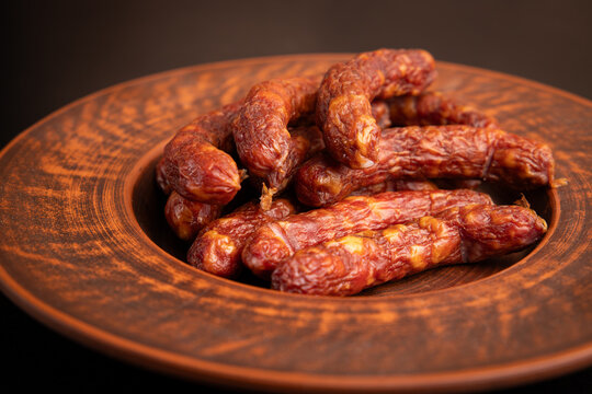Gourmet smoked sausages background closeup with tasty pork meat kolbasa in rustic clay bowl, traditional country farm food over dark surface, horizontal copy space for restaurant menu design.