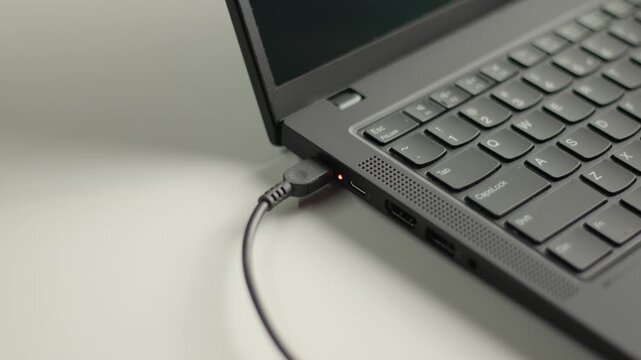 Close up of a man's hand plugging and unplugging a power charger cable into a laptop computer on a white desk