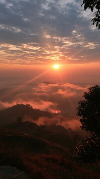 Sunset over a sea of clouds covering rolling hills with warm orange and pink hues painting the dramatic evening sky.