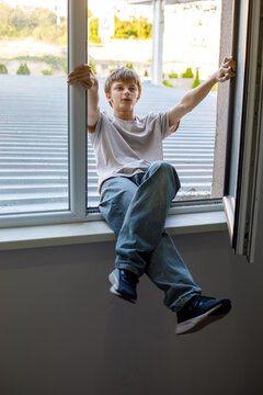 A teenage boy climbs through an open window from the rooftop, moving carefully like a young burglar sneaking into the building