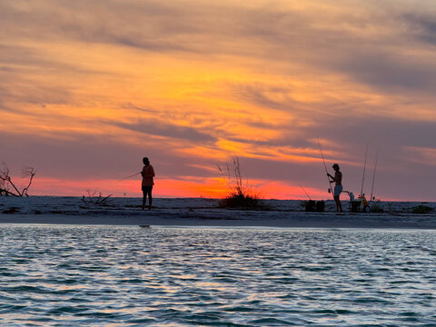 Two people beach fishing during a beautiful sunset with a breathtaking colorful sky.
