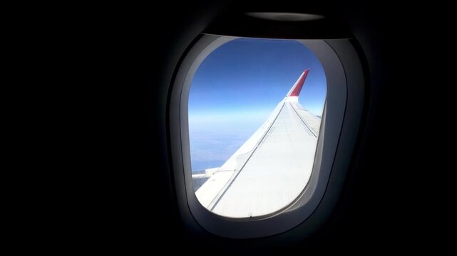Airplane wing visible from passenger window, with a clear blue sky and distant land below, illustrating the journey through the clouds