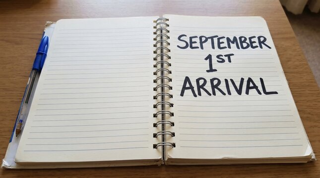 Open spiral notebook with handwritten September 1st Arrival text beside a blue pen on wooden table, marking autumn season start.
