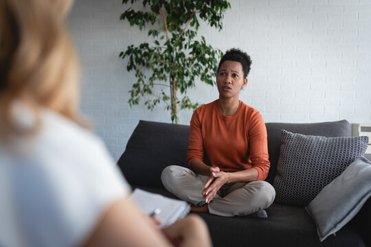 Female therapist listening and taking notes while a woman rests on a sofa and talks during an individual psychotherapy session