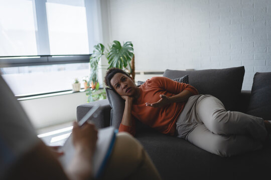 Distressed woman lying on a sofa and talking with a female therapist during an individual counseling session focused on emotional problems