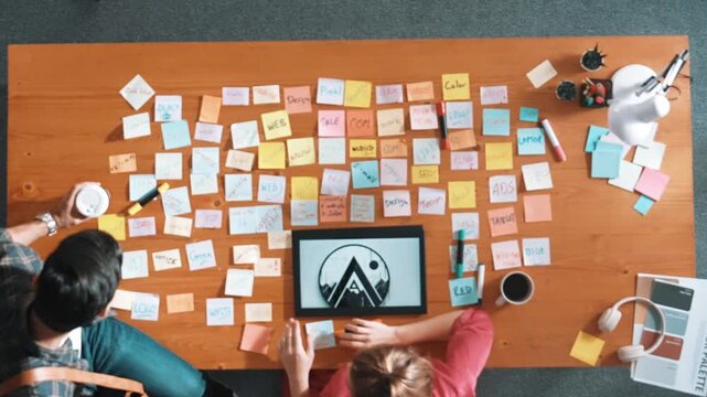 Top view of business people working together to choosing color from color palette. Project manager present idea by using tablet to marketing team while business man looking at logo graphic. Symposium.