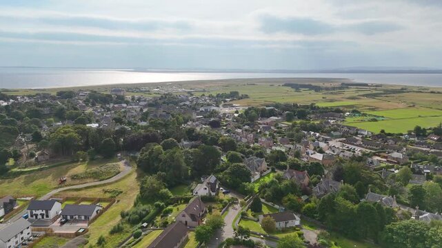High angle aerial drone view of Dornoch town with residential houses, green countryside, and the Dornoch Firth coastline in Sutherland, Scotland