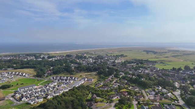 Elevated wide aerial drone video tracking over residential neighborhood housing developments in Dornoch with sandy beach and Dornoch Firth in the background
