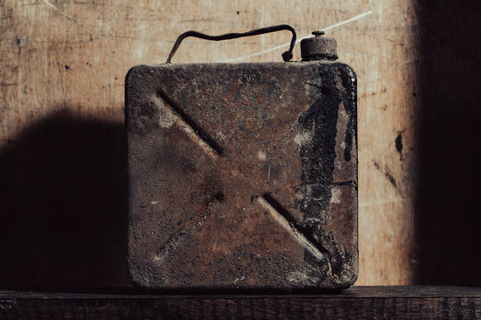 Vintage rusty metal jerrycan on dark rustic wooden background, closeup. Old scratched and rusty fuel canister stands on textured wood surface with dramatic lighting and dark shadows