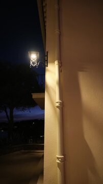 Vintage outdoor lantern casting warm glow and long shadows on a building facade at dusk with a calm lakeside background. Vertical video