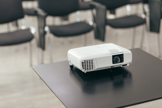 White Projector Rests On Smooth Table Surface. Closeup View Shows Professional Display Equipment In Meeting Room.