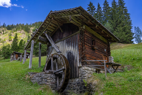 Low-angle view of a historic wooden watermill with an overshot water wheel on a stone foundation in Maria Luggau, Lesachtal, Carinthia, Austria
