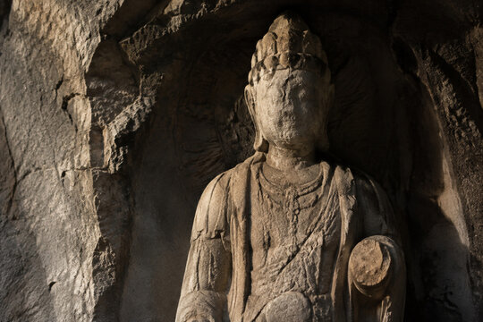 An ancient unfinished stone statue of a deity with a worn face in a rocky alcove.