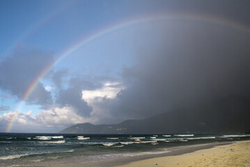 Naklejka premium Beautiful Rainbow Over the Sea and Beach Under Dramatic black Clouds After Rain with Colorful Light Reflections Across the Ocean Horizon in Tortola Caribbean