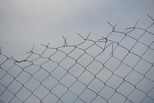 Opening in metallic fence against a blue sky with white clouds. Challenge. uncertainty. breakthrough concept. metaphor. Chain-link, wire netting, wire-mesh, cyclone hurricane fence.