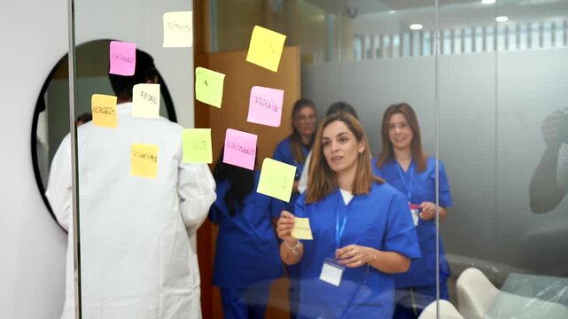 Diverse group of doctors and nurses in a hospital meeting room. Collaborating and sharing ideas by placing colorful adhesive notes on a transparent glass partition during a creative planning session