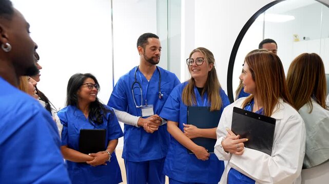 Multiracial group of smiling doctors and nurses in uniform giving a high five, celebrating a successful achievement and showing teamwork spirit in a modern hospital hallway