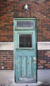 A weathered turquoise wooden entrance door with a decorative transom window and door glass is set into an aged brick wall in Ottawa, Ontario