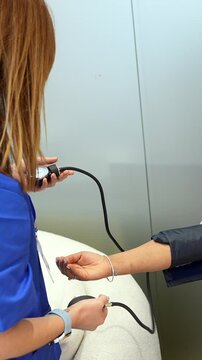 Medical professional taking a smiling woman's blood pressure during a routine check up at a hospital, using an aneroid sphygmomanometer to monitor her cardiovascular health and vital signs