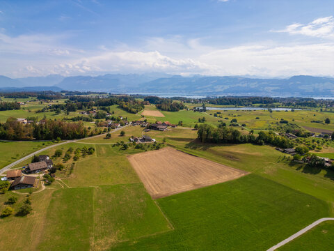 Drone shot of countryside with winding paths and distant Alps in Switzerland