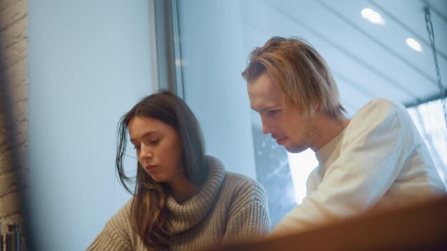 Close up of two people sitting together in casual indoor setting focusing on their upper bodies and interactions. woman wears chunky knit sweater while man is dressed casually both appear