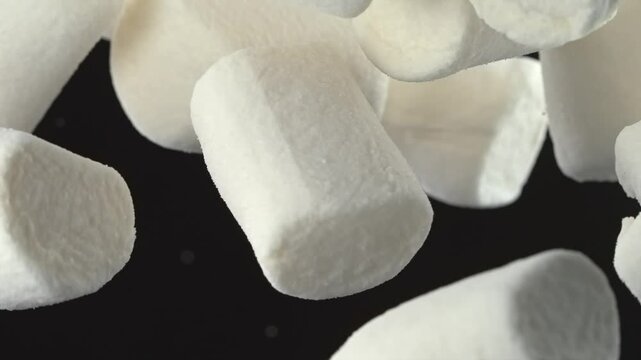 White marshmallows falling through the air in slow motion on black background