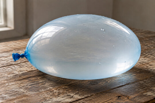 Overfilled translucent water balloon on wooden table, tension and fragility concept