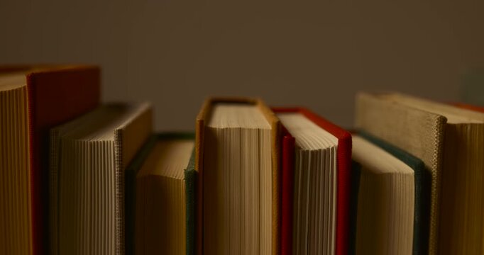 Smooth camera pan right to left with depth parallax effect revealing a row of classic vintage books on a shelf. Detailed close-up shot of book spines and pages in warm, atmospheric lighting.