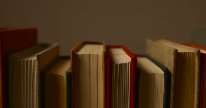 Smooth camera pan right to left with depth parallax effect showing a row of vintage hardcover books standing together on a shelf. Close-up view of book spines, pages, knowledge and warm lighting.