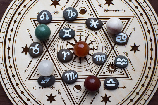 Natural stones and stones with zodiac emblems are arranged on a wooden altar for divination. Fortune-telling, witchcraft, and esoteric spiritual practices.