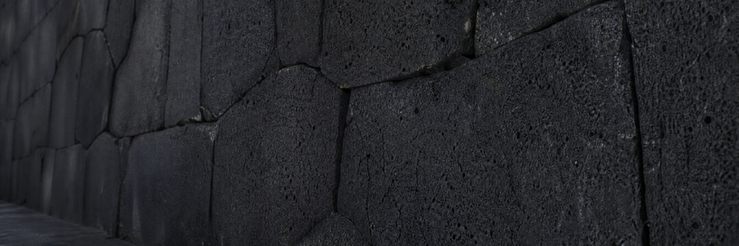 Dark basalt stone wall texture, volcanic rock masonry background, charcoal grey interlocking stone blocks for architectural design