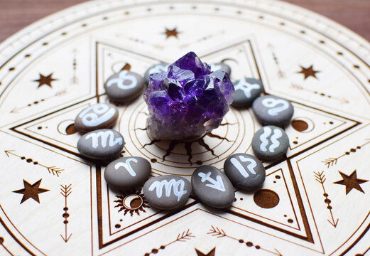 Natural amethyst crystals and stones bearing the emblems of the zodiac signs are arranged on a wooden altar for divination. Fortune-telling, witchcraft, and esoteric spiritual practices.