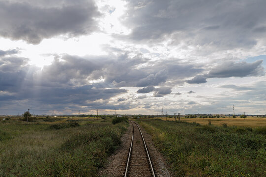 Railway Tracks Stretching Through an Open Rural Landscape Under a Dramatic Cloudy Sky at Sunset