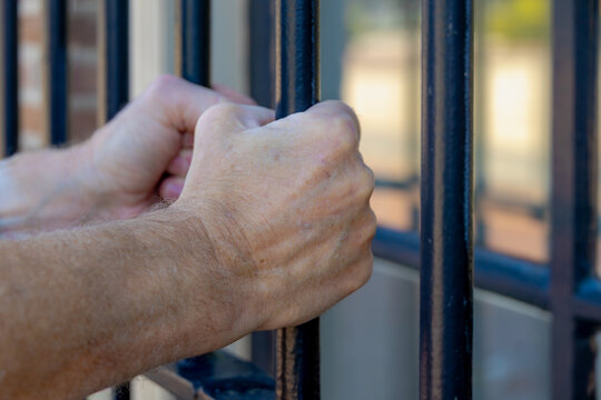 Captivity and loss of freedom, Man's hands holding black prison bars with chains, Hands of a prisoner clutching metal jail bars, Symbol of incarceration, Justice system, Punishment and loss of liberty