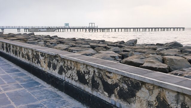 Rocky stone breakwater barrier along coastal sea shoreline near long wooden pier structure
