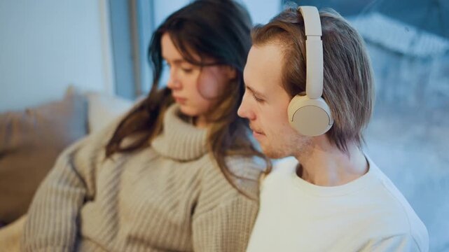 Close up of two people wearing headphones sitting together in relaxed indoor setting. woman wears beige knit sweater while man has on white clothing both appearing calm and focused. Soft