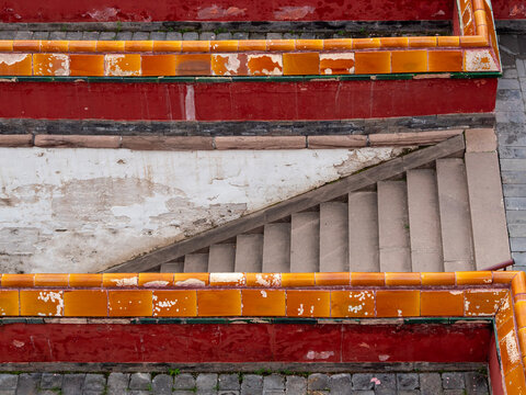 High-Angle Abstract View of Stone Stairs Framed by Tiered Red Walls and Yellow Glazed Tiles