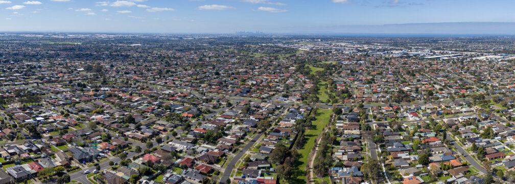 Panoramic aerial view of a suburban drainage reserve and green linear parkland cutting through residential housing estates in Hoppers Crossing, Australia, with distant views of the Melbourne skyline