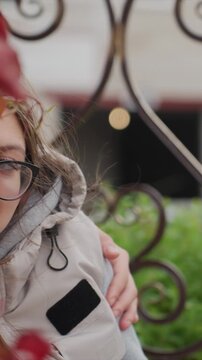 Profile of individual with brown hair wearing glasses. Gentle rustling of plant material behind girl suggests. Outdoor scene includes greenery mixed with colorful foliage