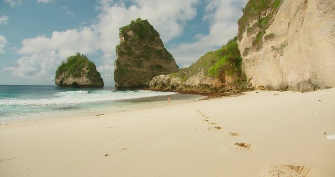 Woman explores sandy shore of Diamond Beach near tall limestone cliffs in Nusa Penida