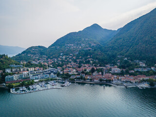 Naklejka premium Aerial drone view of Laveno-Mombello town on the shores of Lake Maggiore in Italy, with picturesque lakeside scenery and Alpine mountains
