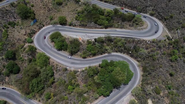 Aerial high-angle drone shot pulling away slowly above vehicles navigating sharp curves on a winding mountain road