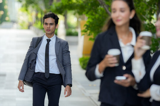A confident multicultural business trio walking the last stretch to the office down a wide green avenue between office towers, an honest snapshot of career life outside the office walls